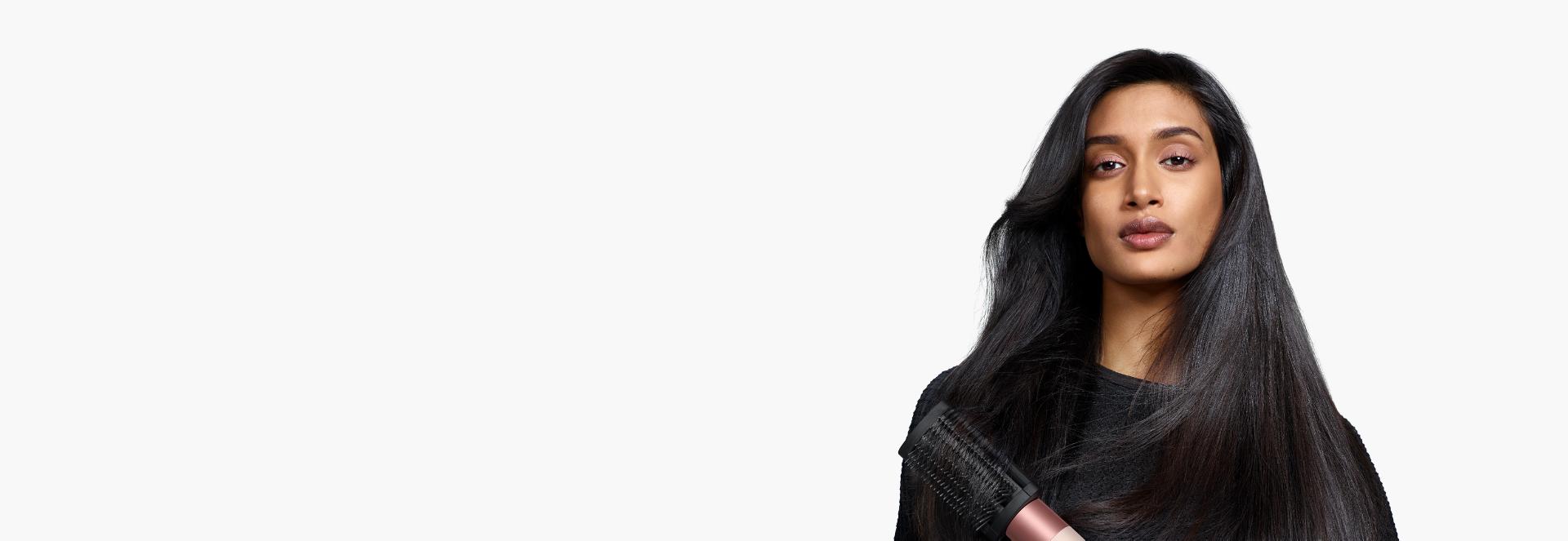 Un model cu părul lung, de culoare închisă, folosește peria fermă pentru netezire pentru a reduce electrizarea.