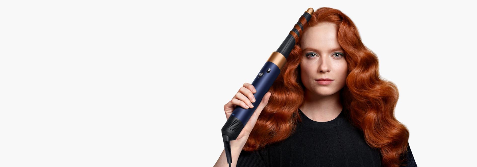 A redhead model with long hair uses the Conical Airwrap barrel to add waves to her hair.