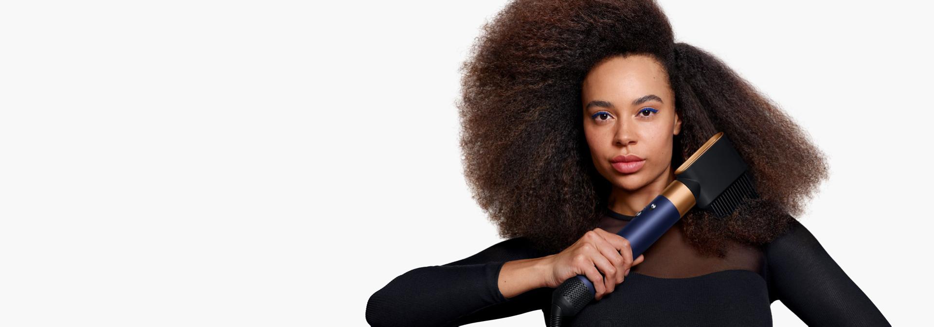 A model with coily hair uses the Wide-tooth comb attachment to shape and lengthen her natural hair.