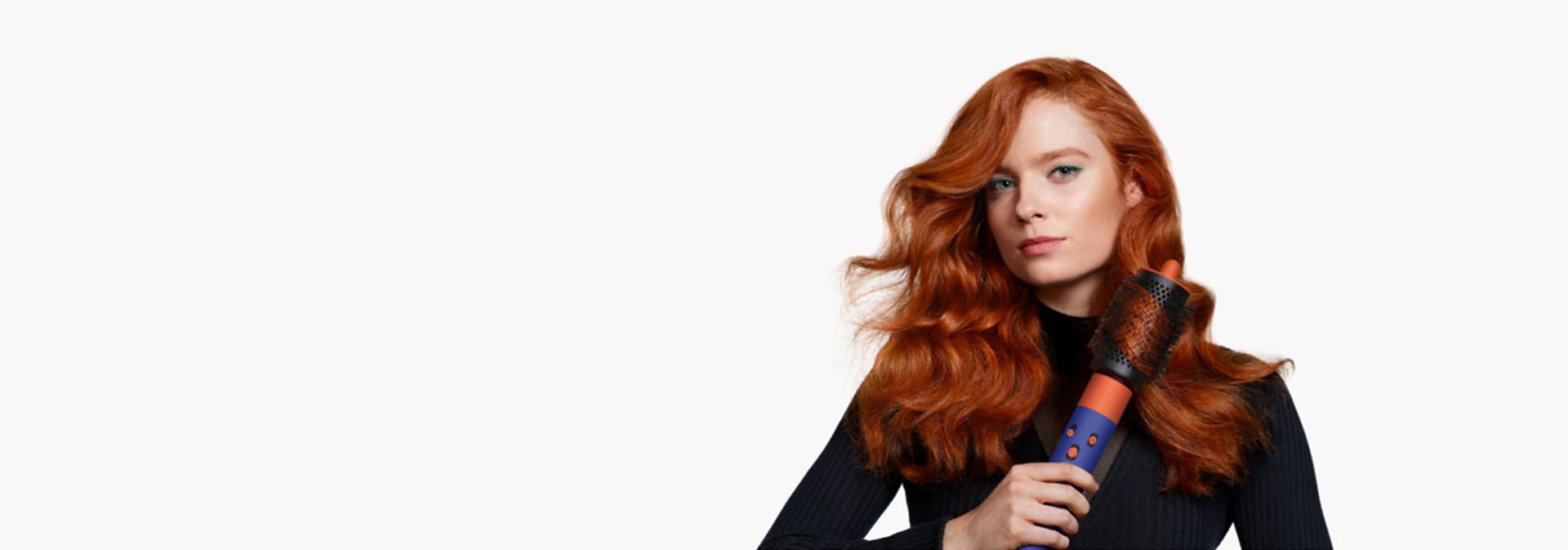 A redhead model with wavy hair uses the Large round volumising brush attachment to add volume and body to her hair.