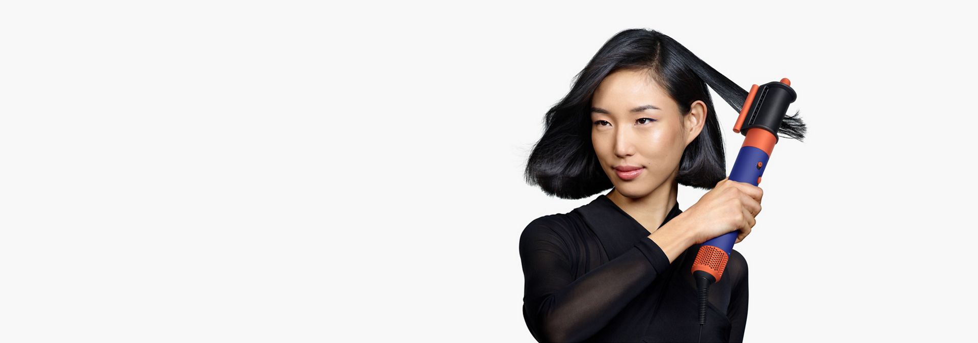 A model with medium length black hair uses the Dryer+Flyaway smoother attachment to smooth her hair style.