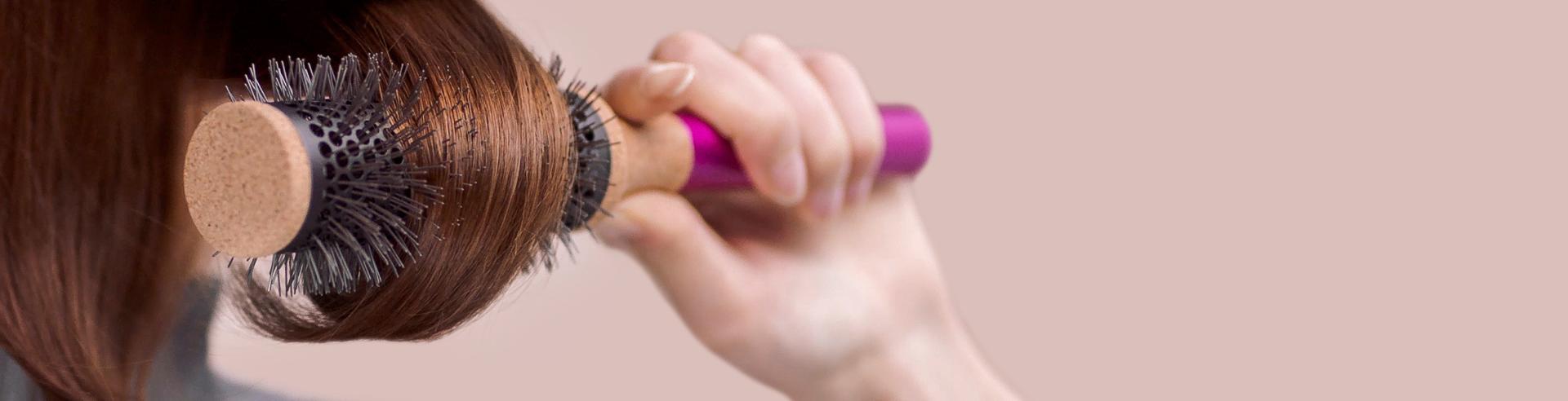 عارِضة تَستخدم فرشاة مستديرة على خصلة شعر.