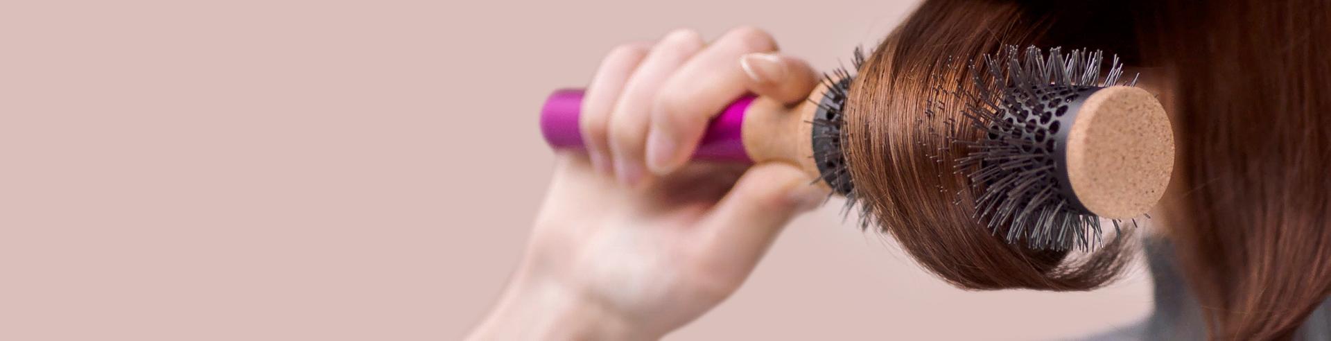 A model using a round brush on a tress of hair.