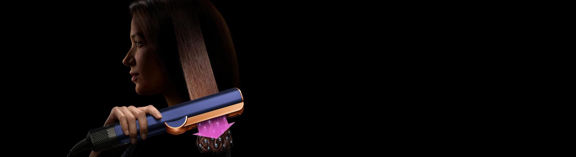 A woman using a Dyson Airstrait straightener to dry and straighten a tress of her hair.