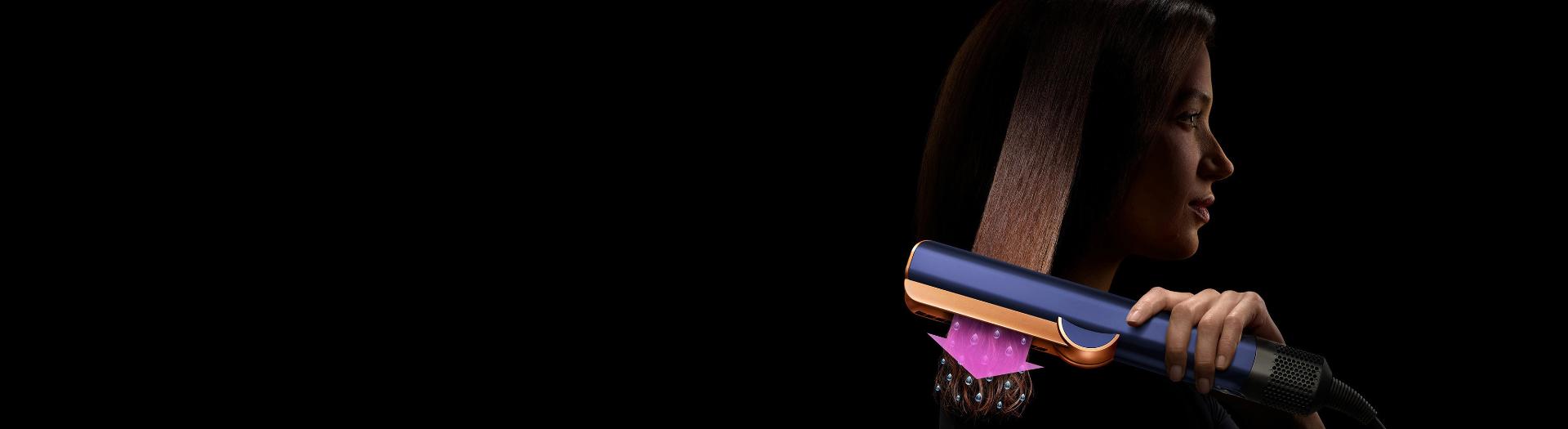 A woman using a Dyson Airstrait straightener to dry and straighten a tress of her hair.