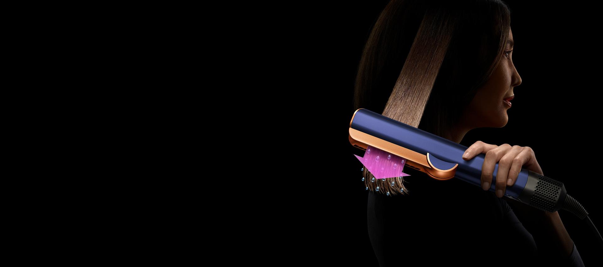 한 갈래 모발에 다이슨 에어스트레이트 스트레이트너를 사용하고 있는 여성. 분홍색 화살표와 물방울 모형을 통해 모발을 스트레이트하는 동시에 건조하고 있는 모습을 나타냅니다.