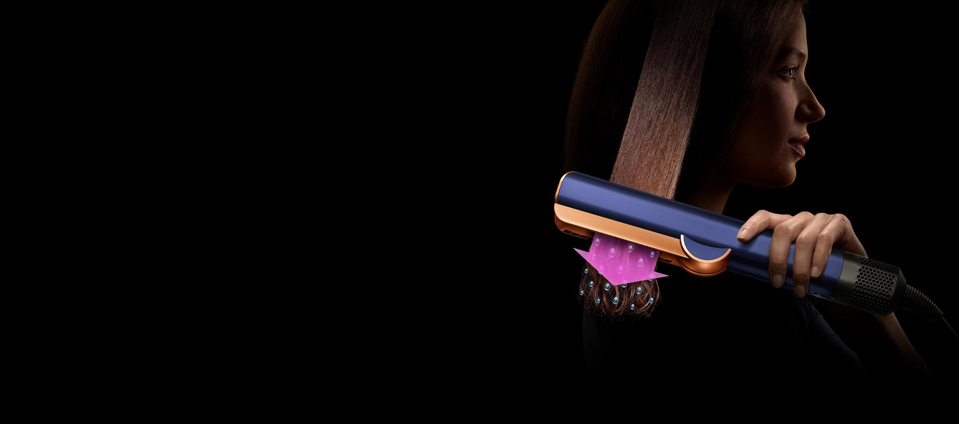 Una mujer utiliza la alisadora Dyson Airstrait en un mechón de cabello. Una flecha rosa y unas gotitas indican que el cabello se está secando mientras se alisa.