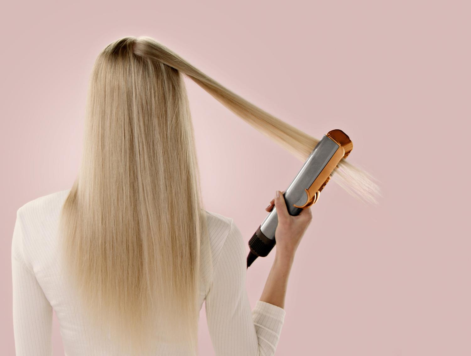 A model uses a Dyson Airstrait to straighten a tress of hair.