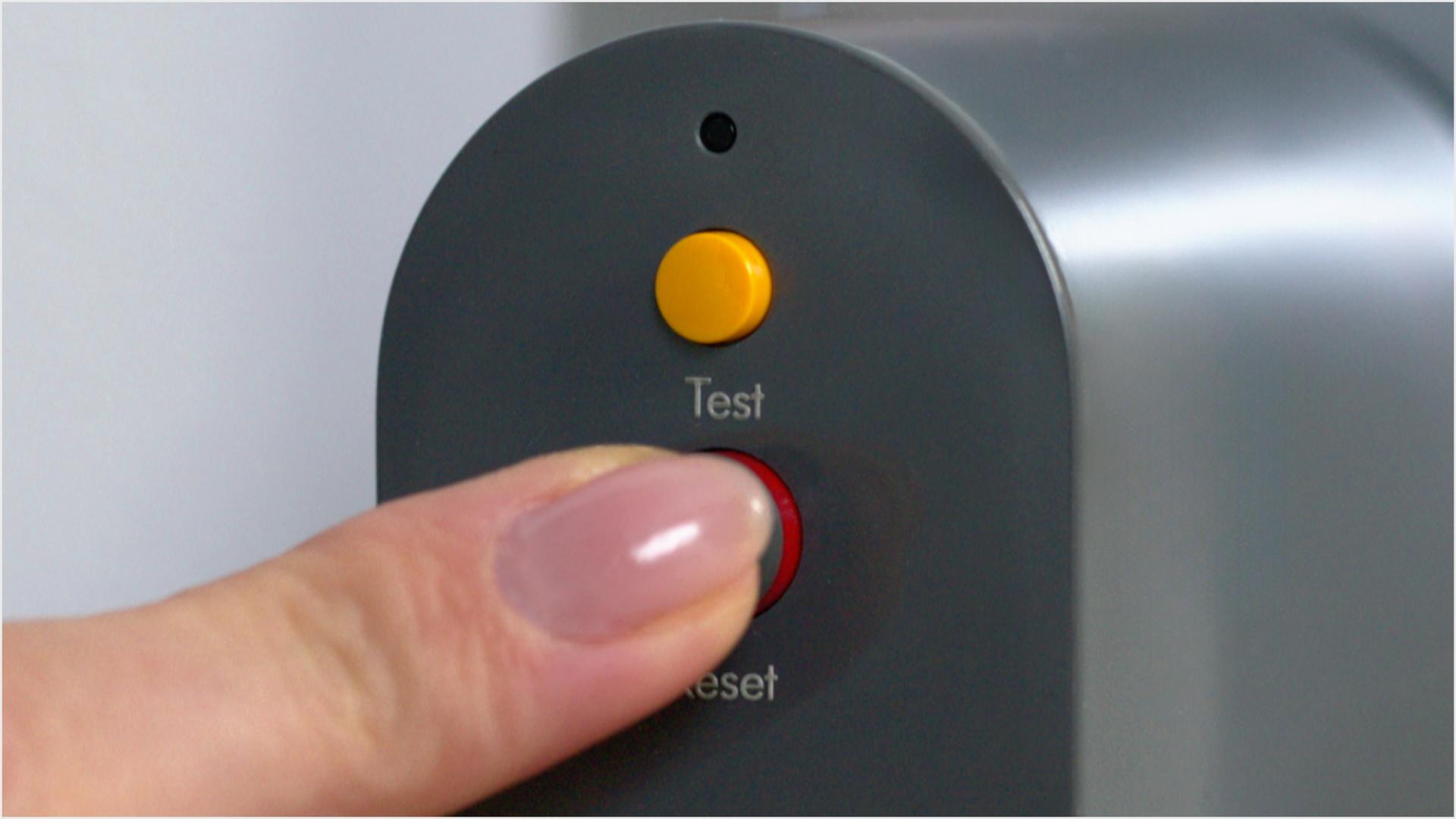 A finger is shown pressing the reset button on the PRCD plug