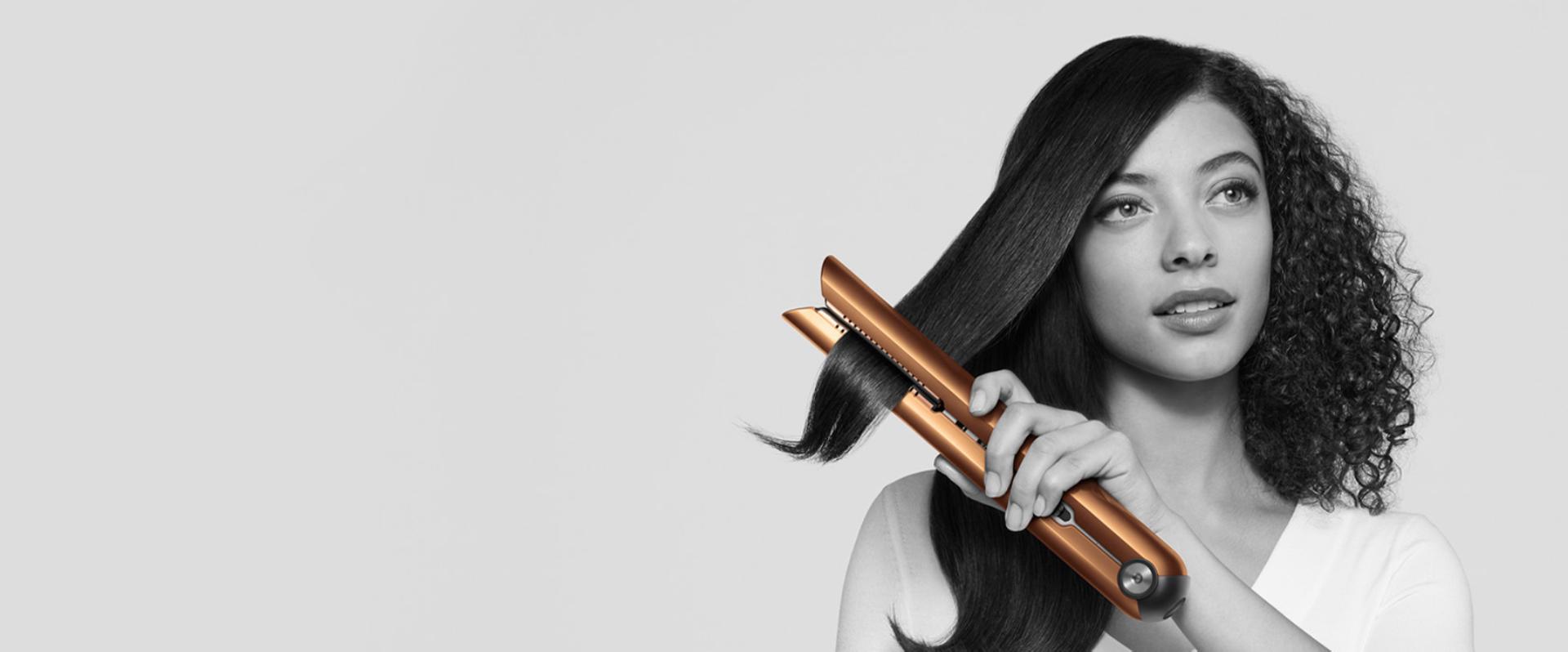 Mujer alaciándose el cabello con la alaciadora Dyson Corrale™