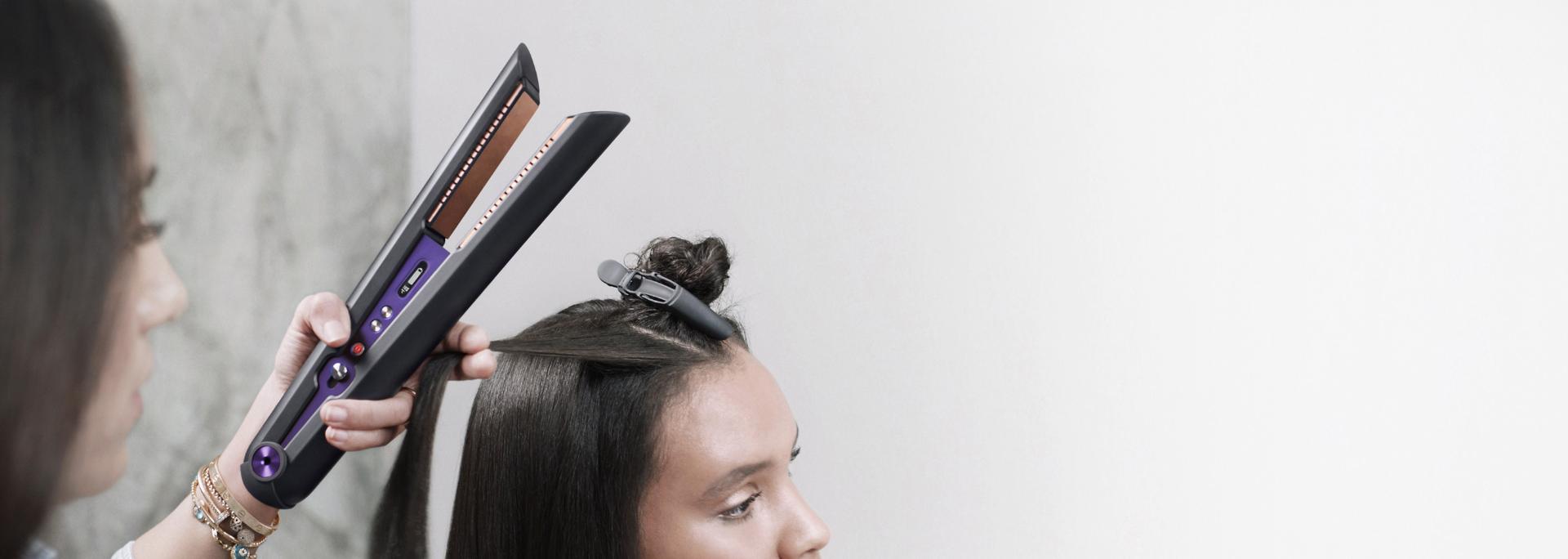 صورة مُقرَّبة من مُصفّفة شعر محترفة تستخدم جهاز تمليس الشعر Dyson Corrale