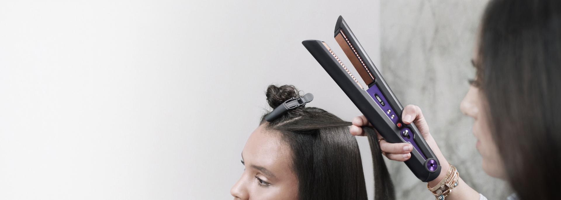 Közelkép valakiről, aki Dyson Corrale hajvasalóval formázza a haját.