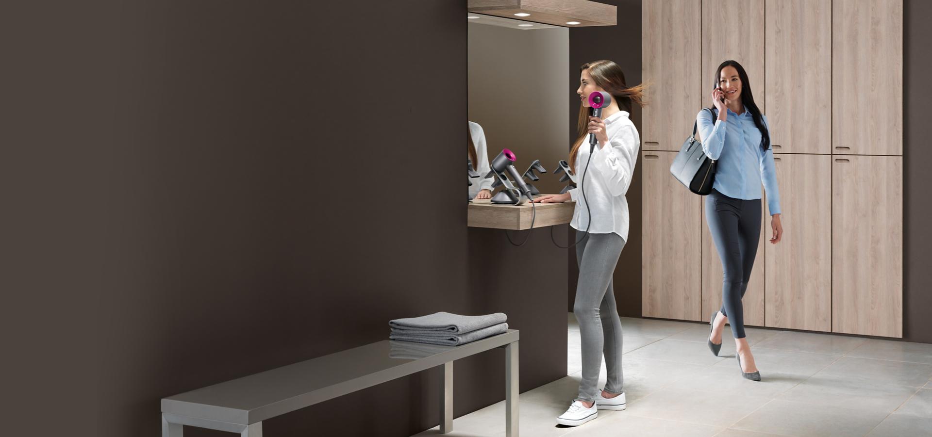 Two women in a changing room. One using Dyson Supersonic.