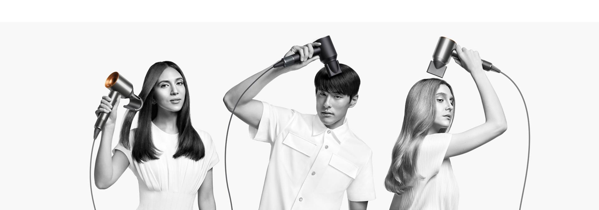 Two women dry their hair with the Dyson Supersonic hair dryer. The woman on the left uses the Flyaway attachment to smooth her straight long hair and the woman on the right uses the Diffuser attachment to shape her coily short hair.