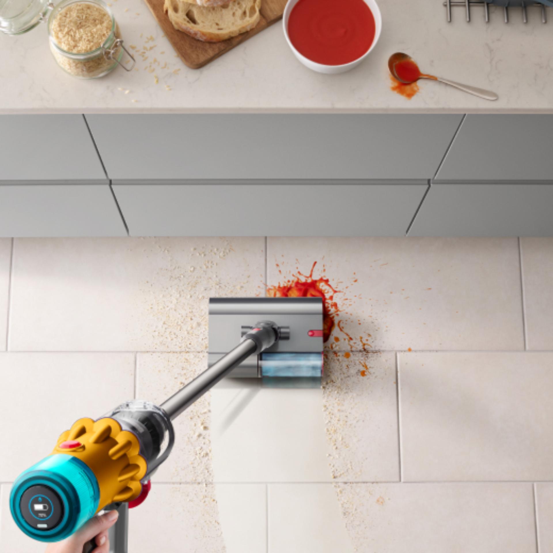 The Dyson Submarine wet roller head is used to clean a food spill in a kitchen.