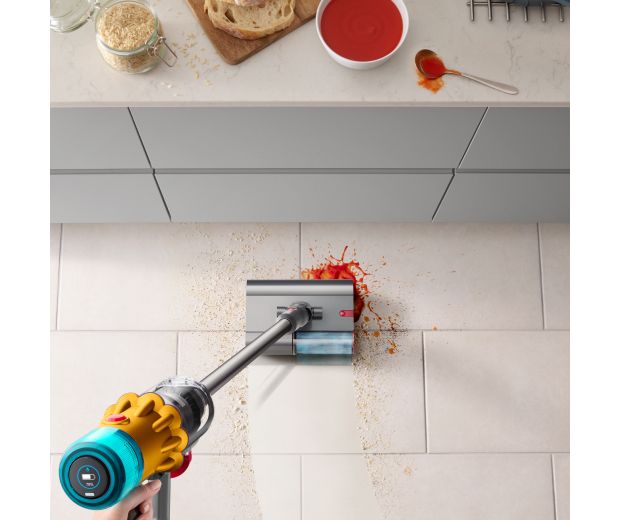 The Dyson Submarine wet roller head is used to clean a food spill in a kitchen.