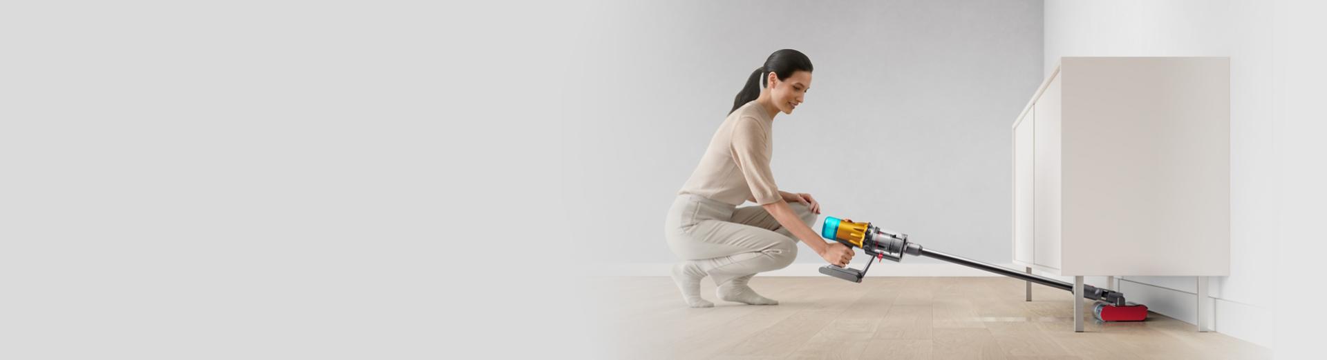 A Dyson V12 vacuum with the Submarine wet roller head is used to clean under a low cabinet.