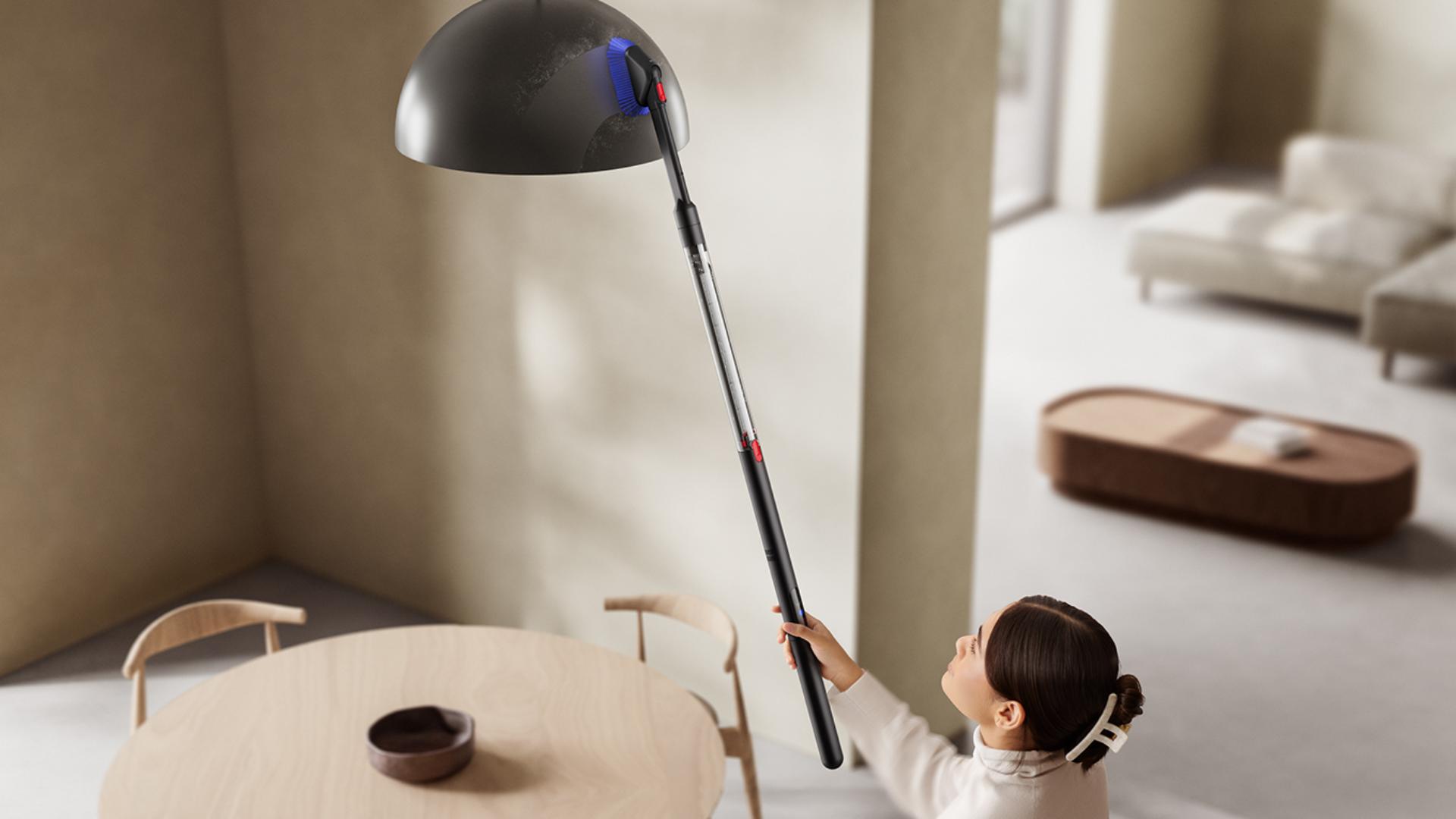 A Dyson PencilVac készüléket a kombinált résszívó fejjel használják egy magasan elhelyezett lámpaernyő tisztítására.