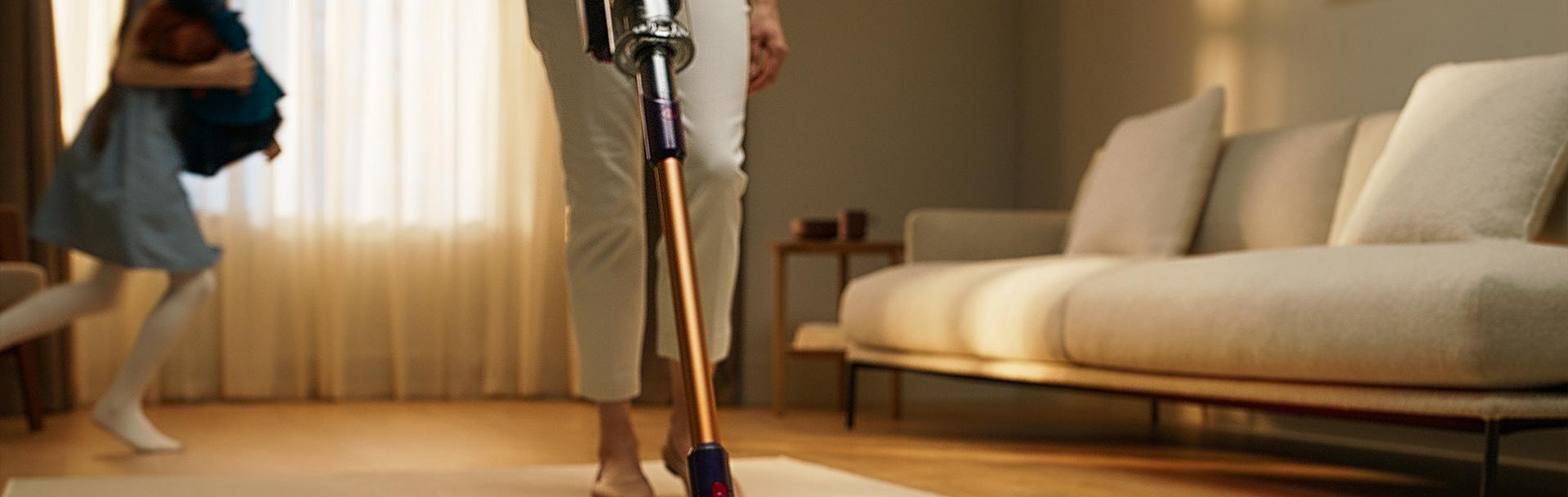 A person uses a Dyson vacuum cleaner with the Digital Motorbar cleaner head to clean debris from a carpet