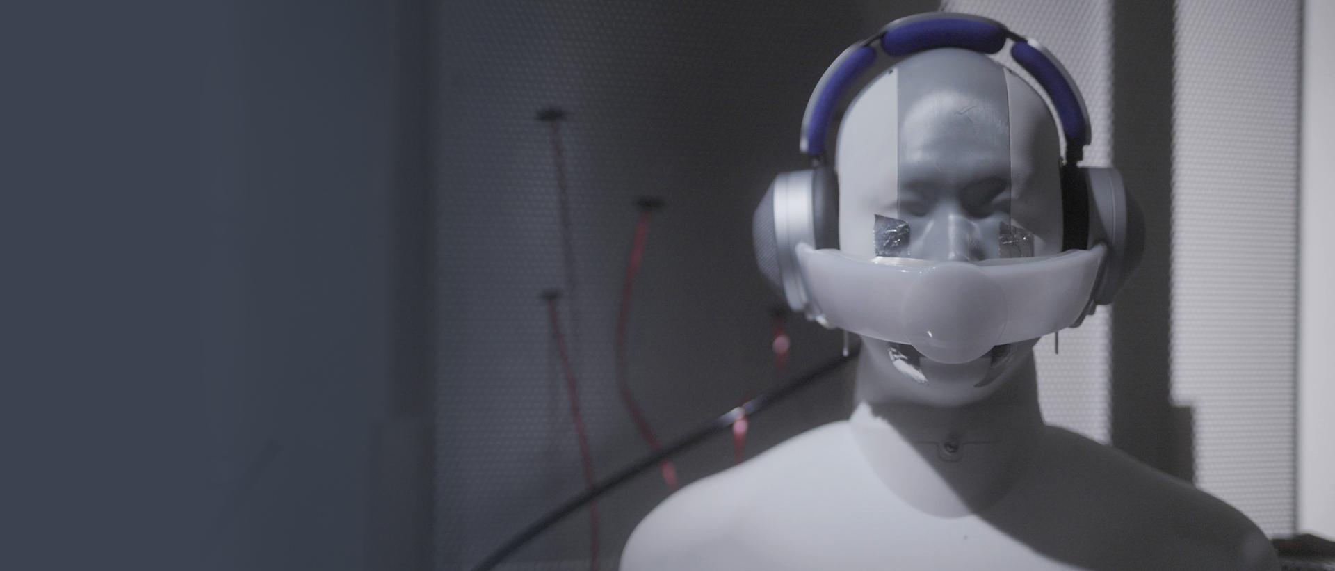Manikin wearing prototype headphones, with visor across nose and mouth