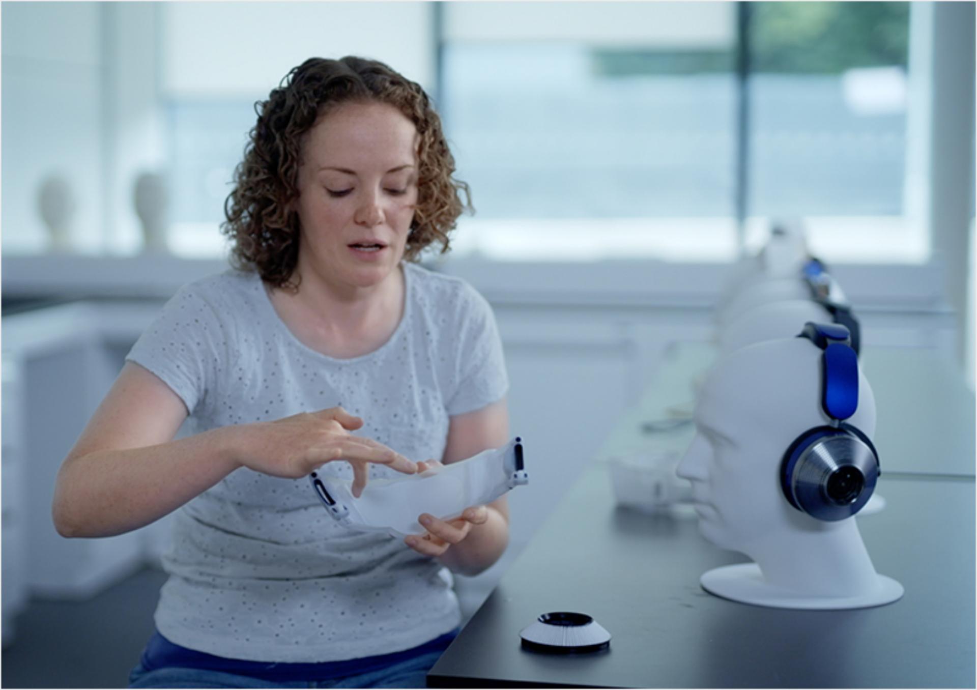 Engineer holds contact-free visor in her hands in front of mannequin wearing full headphones.