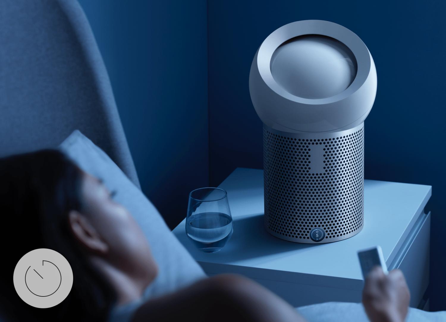 Femme dans son lit utilisant sa télécommande pour régler le minuteur de mise en veille du Dyson Pure Cool Me🅪