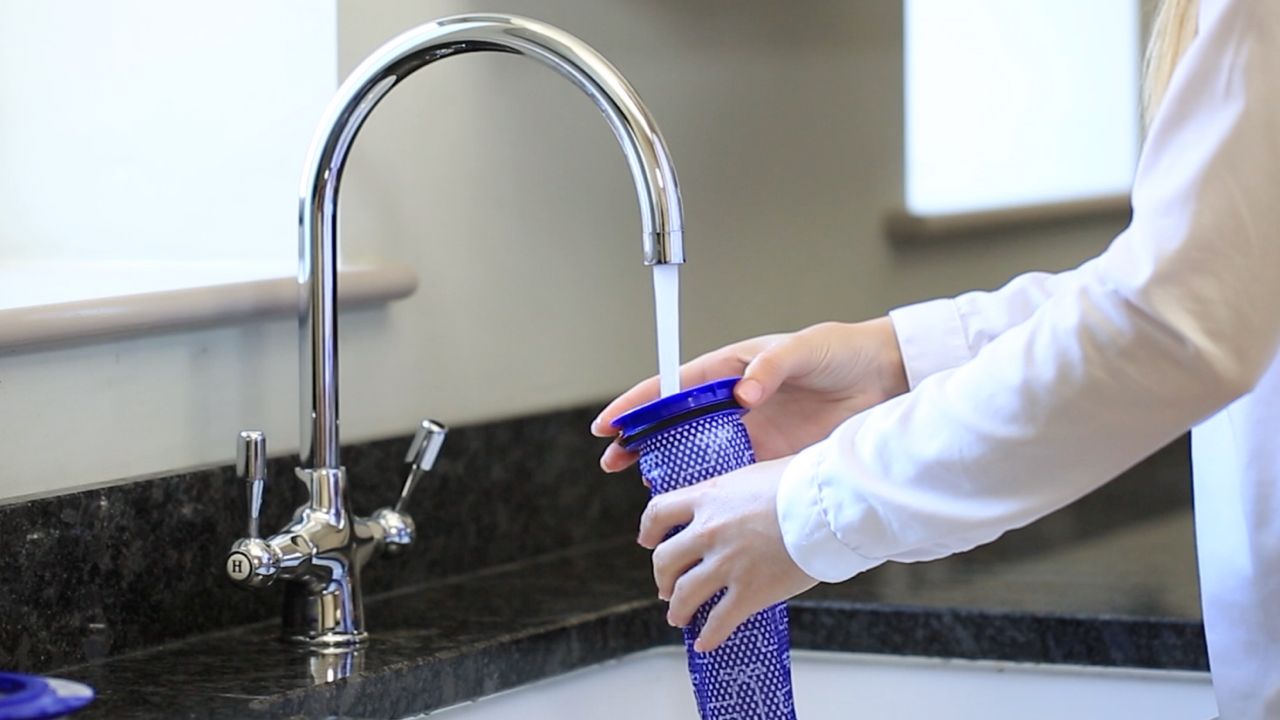 A person cleans their Dyson Car+Boat filter under a running tap.