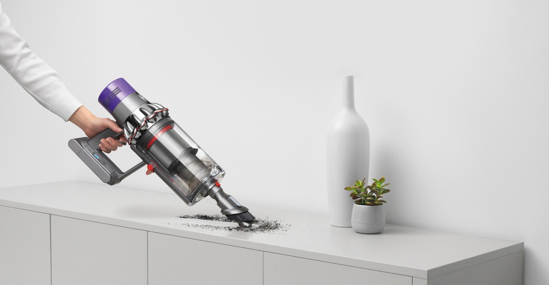 مكنسة Dyson Cyclone V10 في مهمة تنظيف تحت أريكة رمادية.