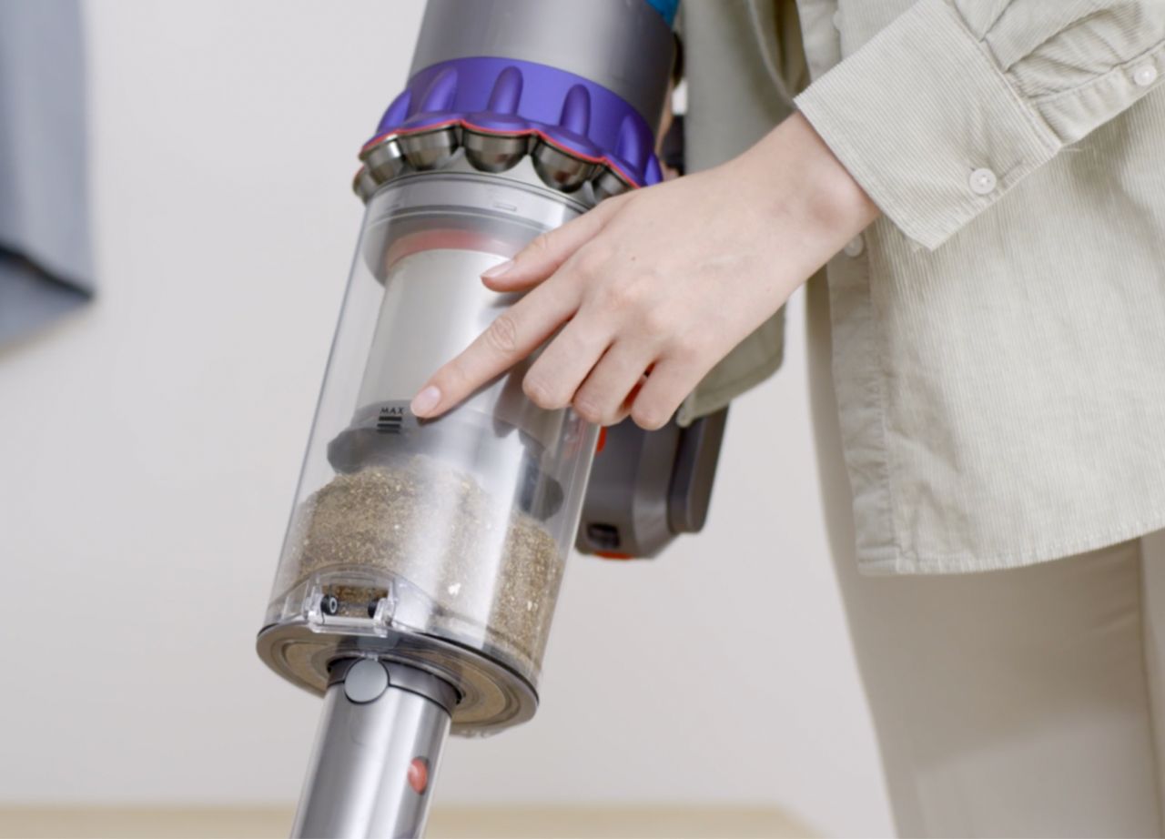 Video still of a woman's hand pointing to the dust level inside a Dyson transparent vacuum bin.