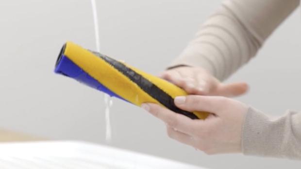 أيدي مستخدم بينما تغسل عمود الفُرَش تحت الصنبور.