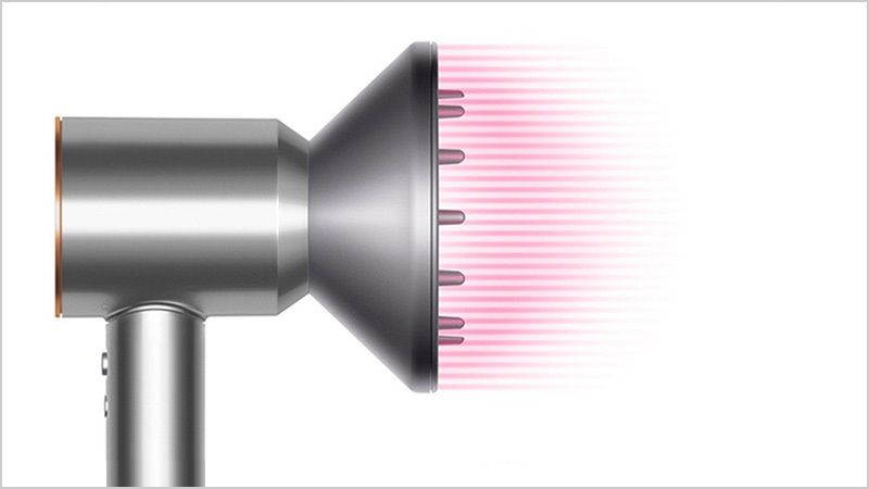Dyson Supersonic™ヘアードライヤーのコールドショットボタンを押してスタイルをセットする女性