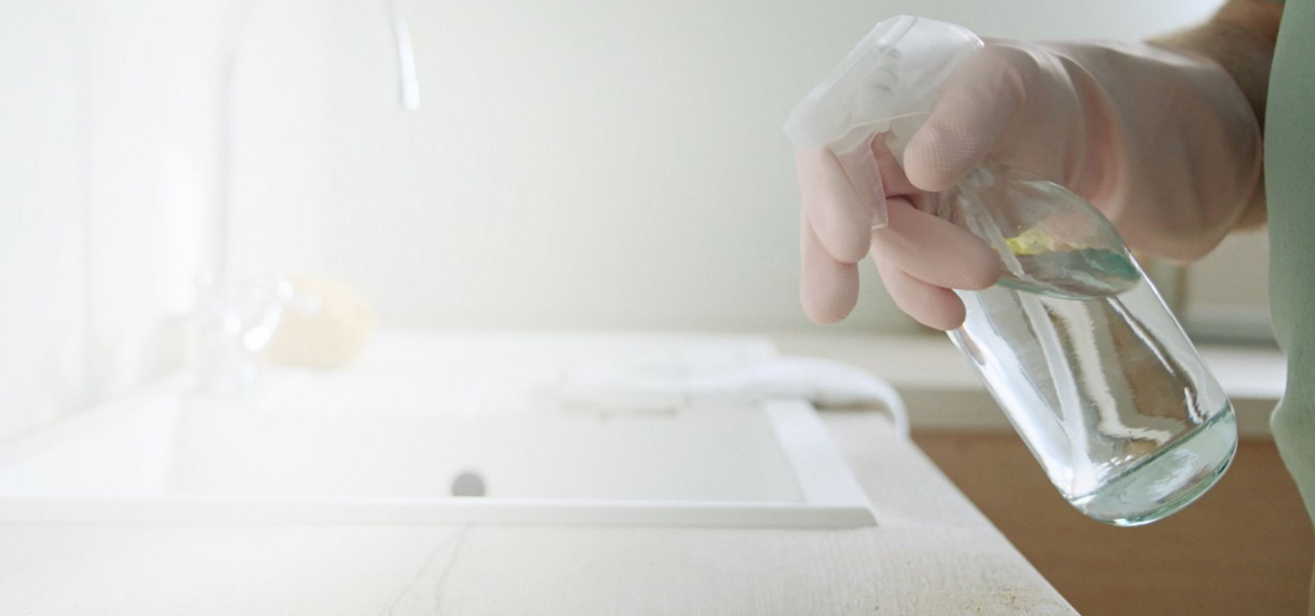 A gloved hand spraying a cleaning product onto a kitchen sink area.