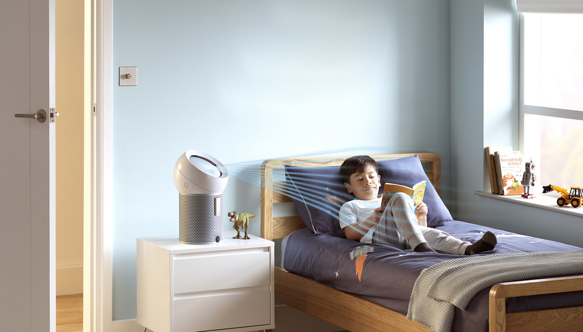 Ein Junge liest auf seinem Bett, während ein Dyson Pure Cool Me™ Luftreiniger einen kühlenden Luftstrom auf ihn richtet