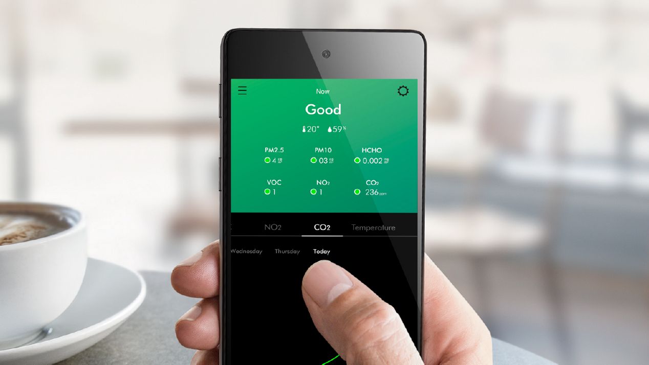 Close-up of a hand holding a smartphone, the screen shows the levels of pollutants in their home. 