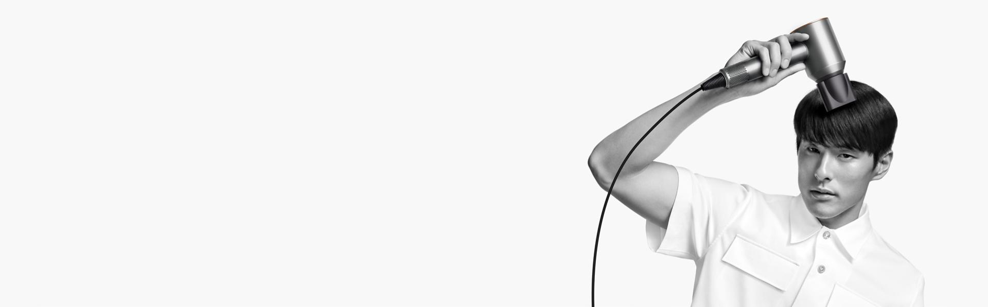 The Dyson Supersonic Origin hair dryer used by a model with short dark hair.