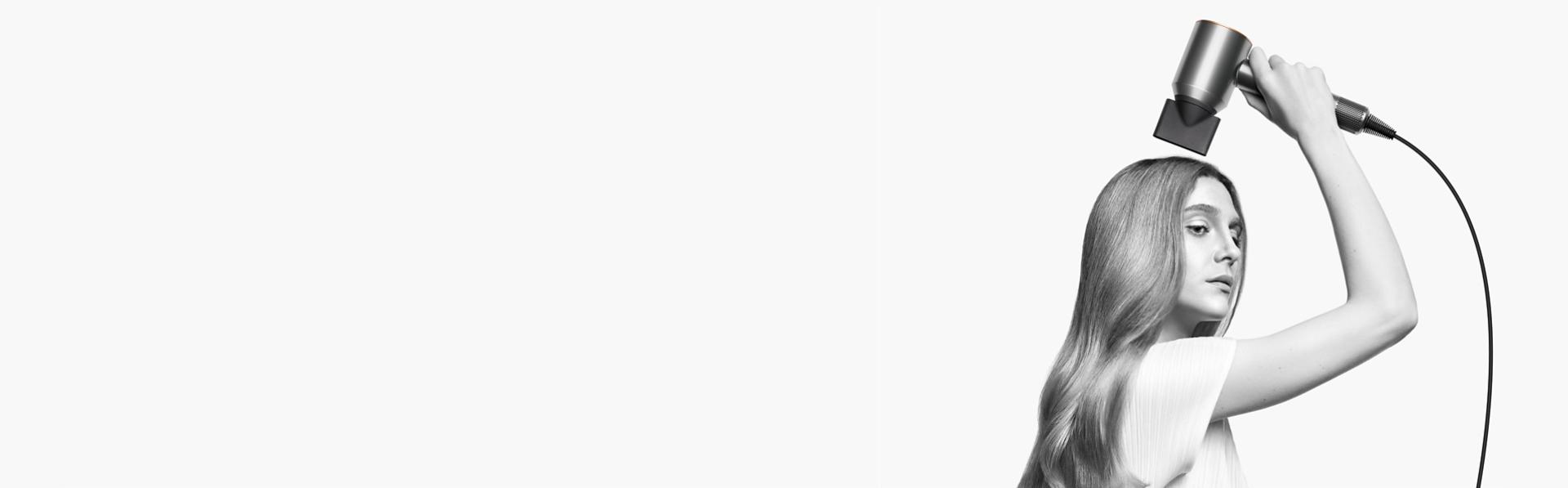 Modelka s krátkymi tmavými vlasmi používa sušič vlasov Dyson Supersonic Origin.