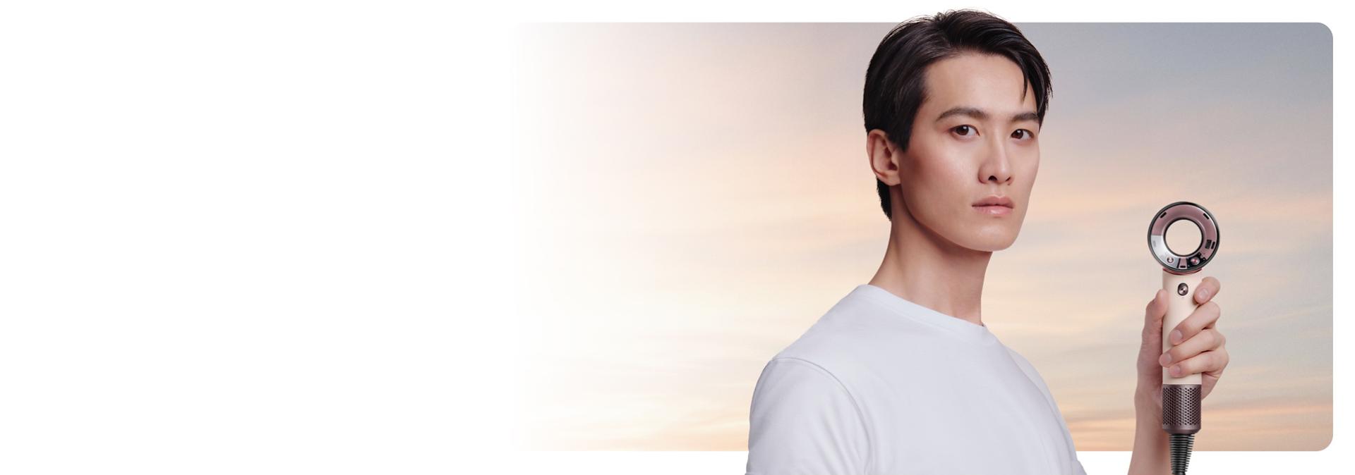 Model holds the Dyson Supersonic Travel hair dryer to one side.