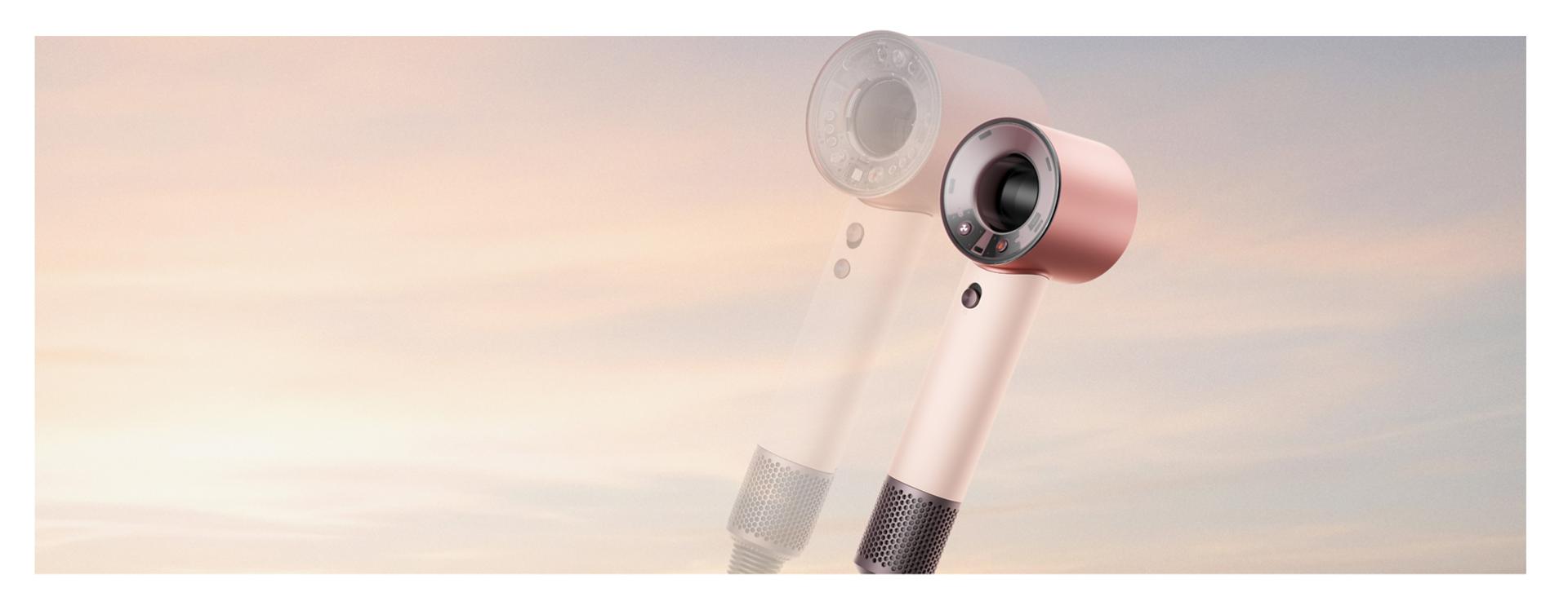 Dyson Supersonic Travel hair dryer in front of a sunrise and a transparent Dyson Supersonic Nural hair dryer.