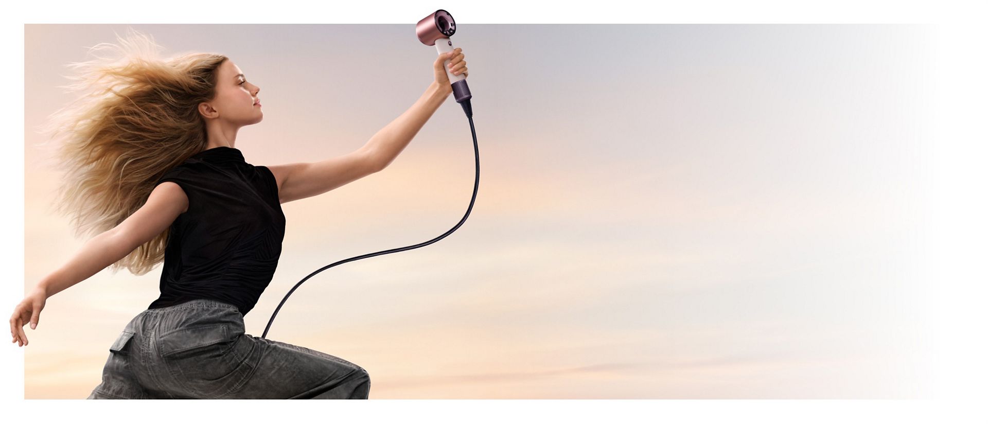 A jumping female model in mid-air holding the Dyson Supersonic Travel hair dryer.