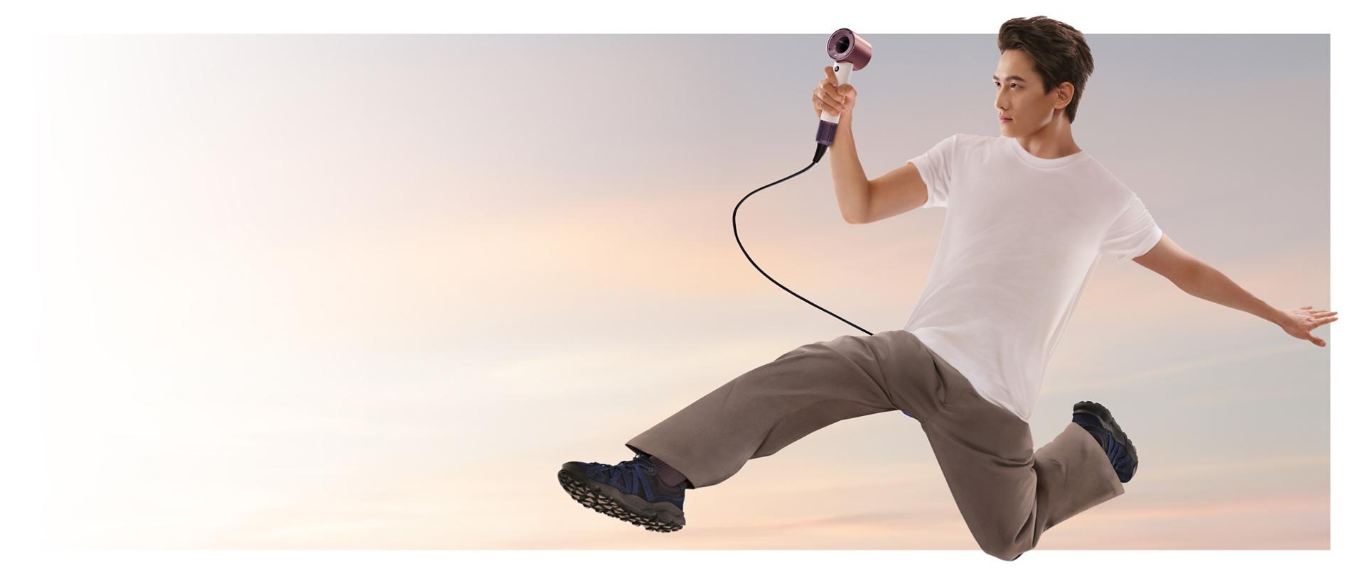 A jumping male model in mid-air holding the Dyson Supersonic Travel hair dryer.