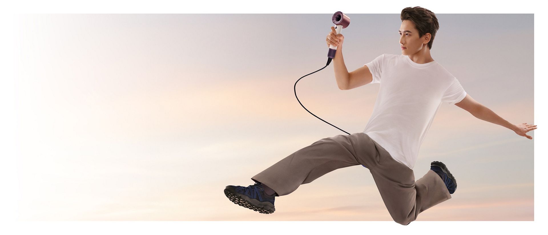 A jumping male model in mid-air holding the Dyson Supersonic Travel hair dryer.