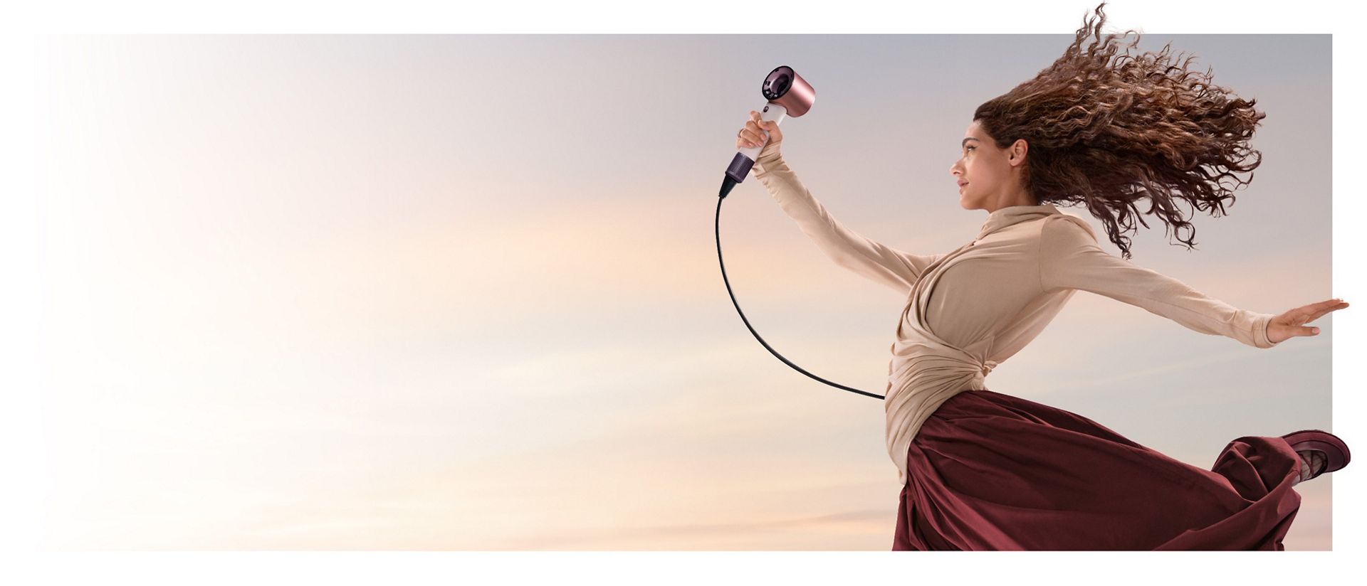 A jumping female model in mid-air holding the Dyson Supersonic Travel hair dryer.