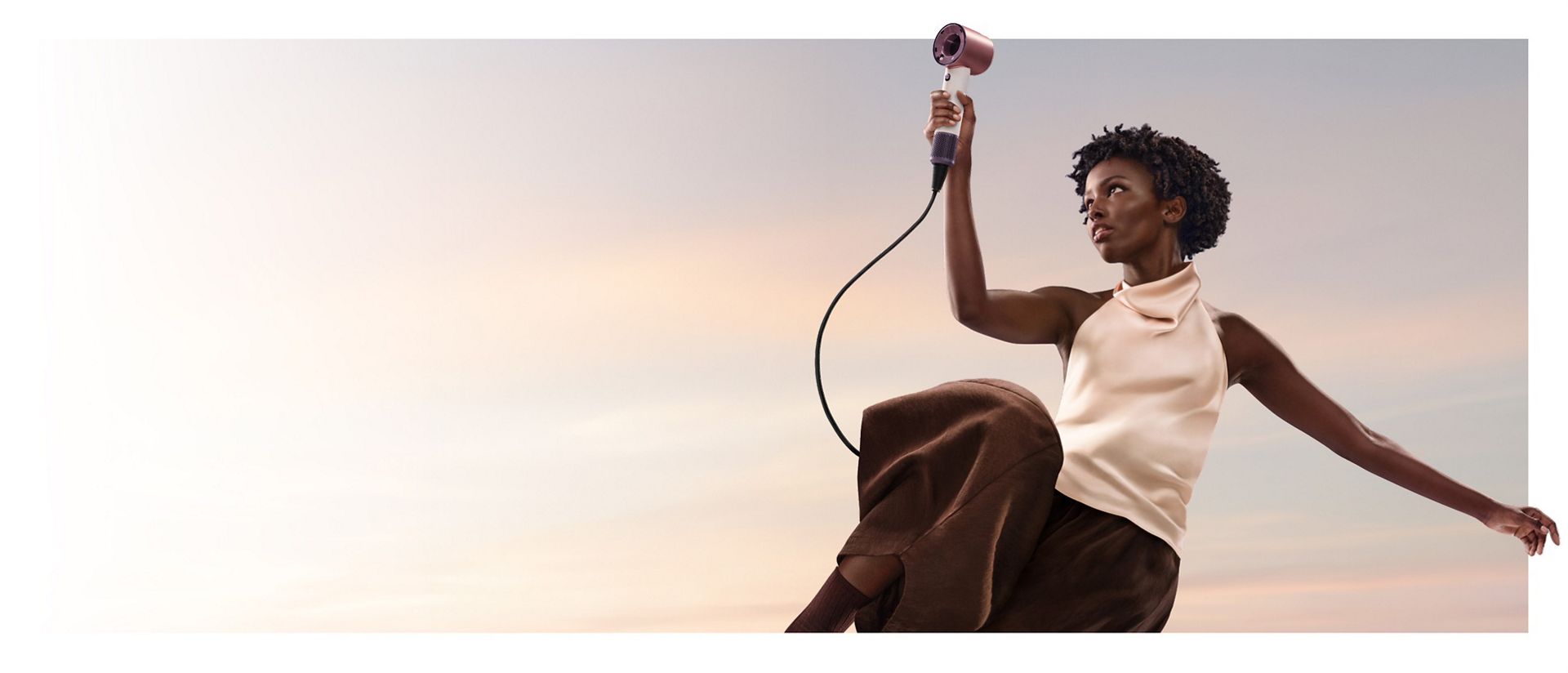 A jumping female model in mid-air holding the Dyson Supersonic Travel hair dryer.