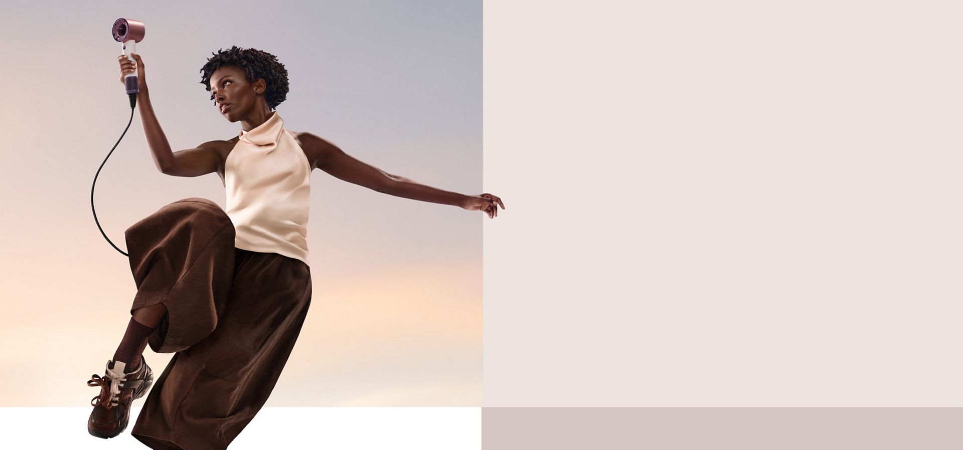 A jumping model in mid-air holding the Dyson Supersonic Travel hair dryer.