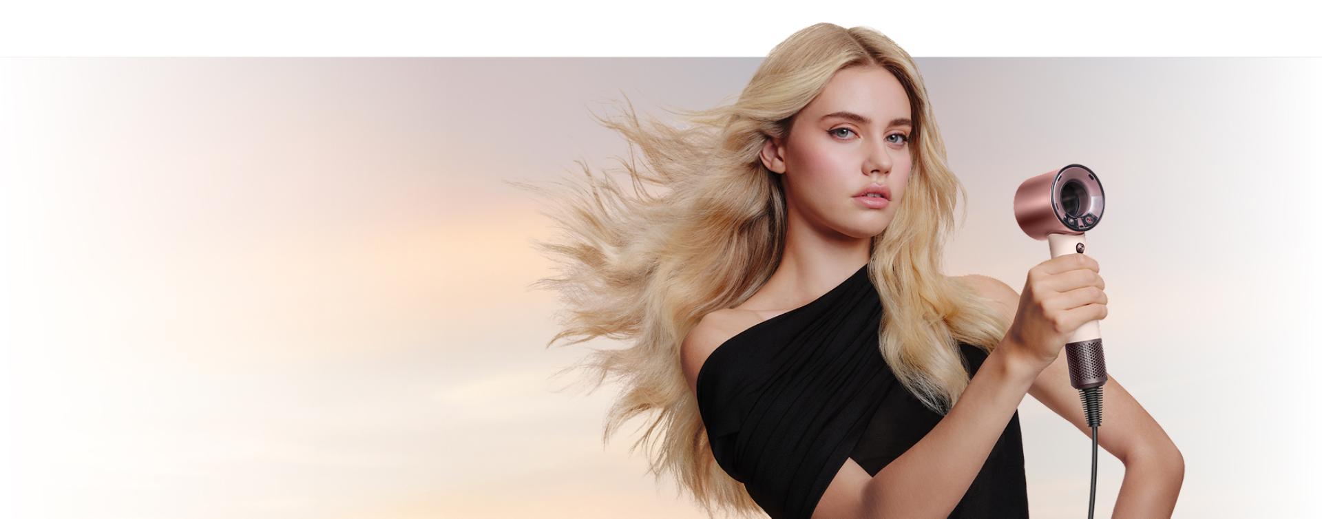 A female model with straight and wavy styling dries her blonde hair with the Dyson Supersonic Travel hair dryer.