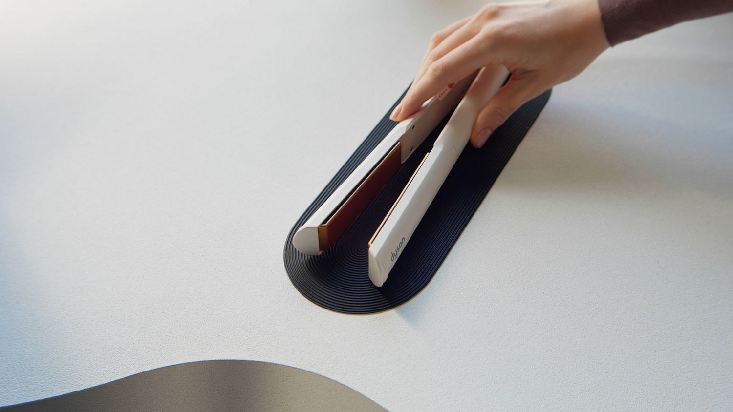 Model's hand placing the Dyson Corrale CoolShine hair straightener on the non-slip heat mat.