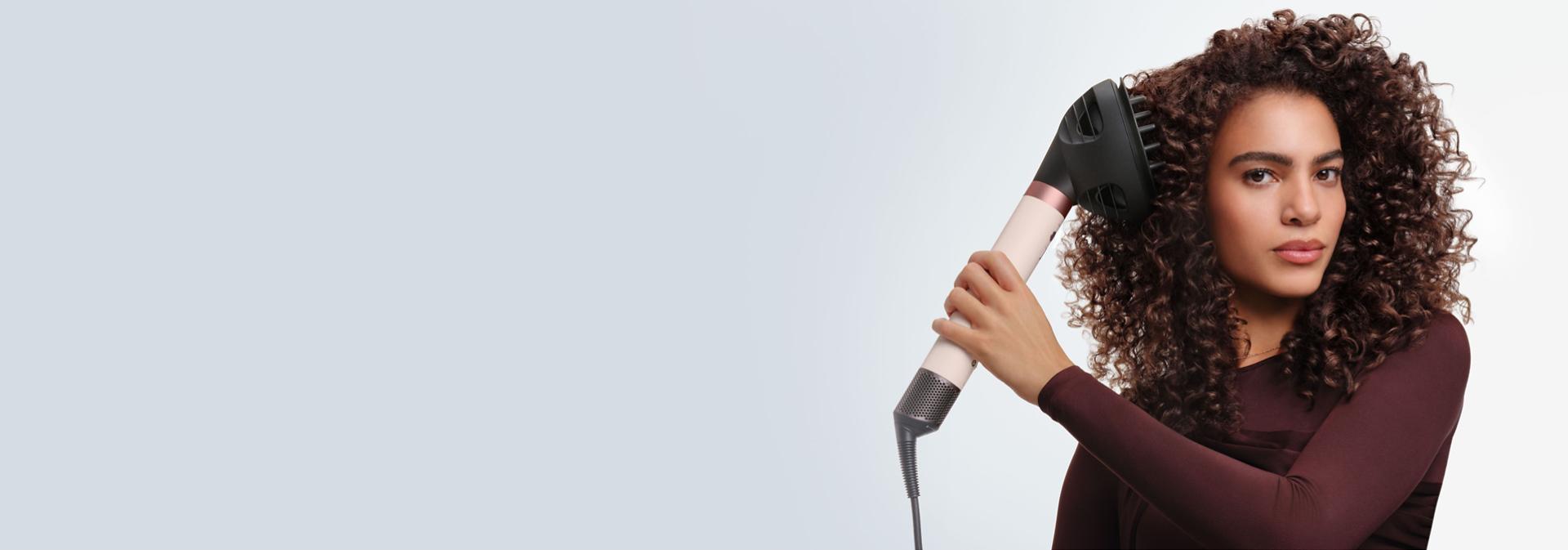 Modelka si suší vlasy pomocí multifunkčního stylingového přístroje a fénu Dyson Airwrap Co-anda2x.