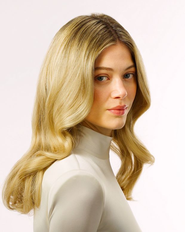 A model with long, wavy blonde hair wearing, turned sideways against a light background