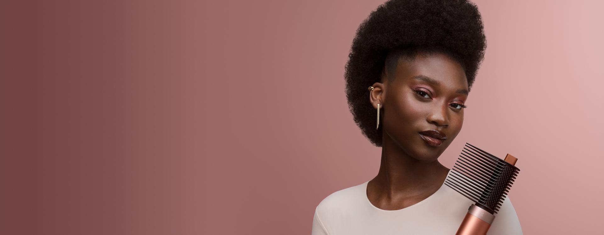 Dyson Airwrap Co-anda2x multi-styler and dryer with the Tension Comb 2x attachment held by a model.