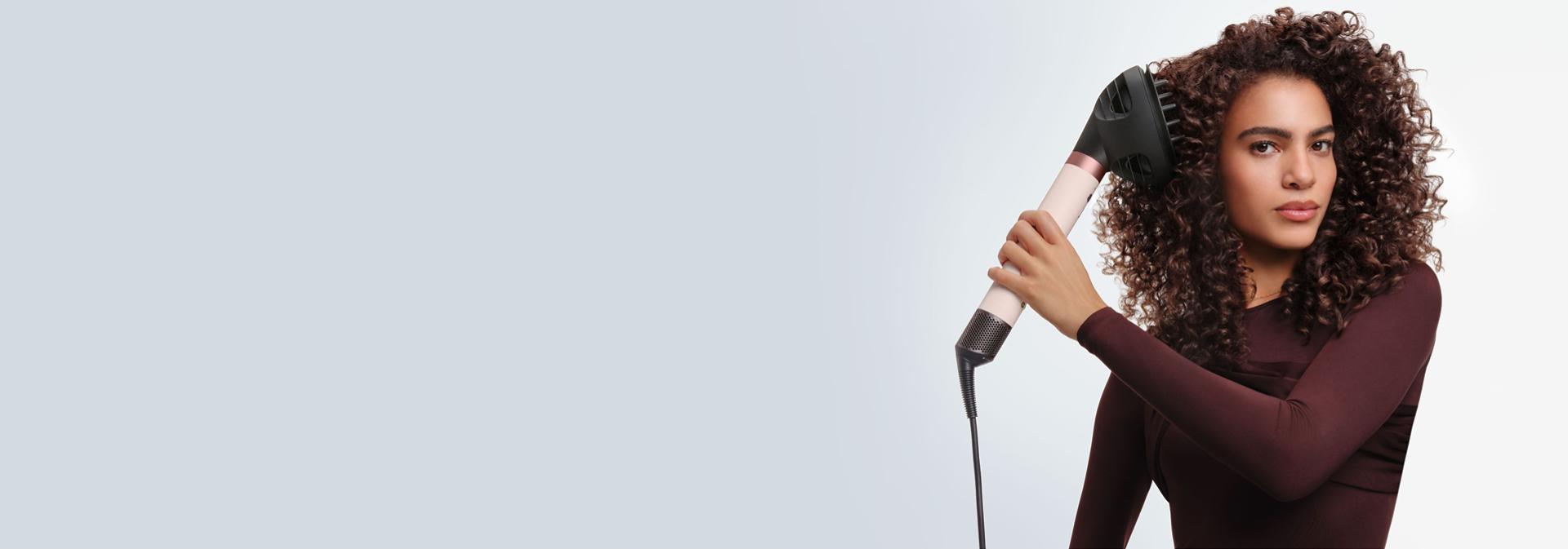 Model styles her hair with the Dyson Airwrap Co-anda2x multi-styler and dryer.